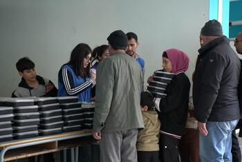 WFP distributes food aid to displaced families sheltering in a public school in Tariq Jdide, Beirut, Lebanon. Volunteers hand out stacks of food boxes to adults and children.
