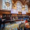 UN Secretary-General António Guterres speaking at a podium during a solemn sitting at the International Court of Justice to celebrate its 80th anniversary. Other dignitaries including King Willem-Alexander of the Netherlands, ICJ President Iwasawa Yuji, and UN officials are seated in the Great Hall of Justice.