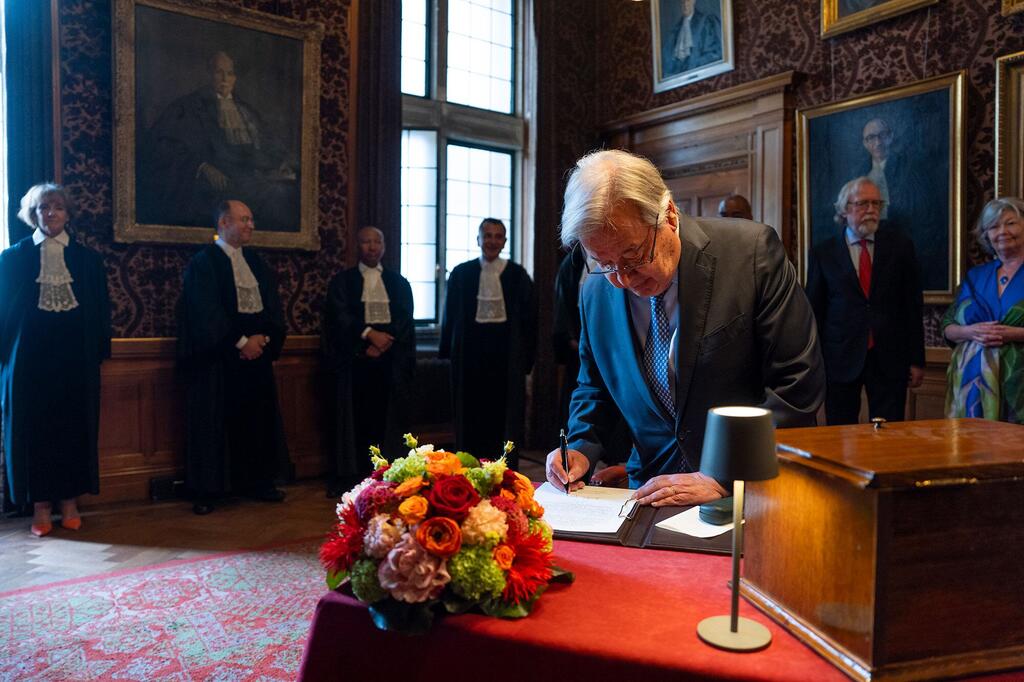 António Guterres signe un livre commémoratif à la Cour internationale de Justice pour son 80e anniversaire, entouré de juges en robe.