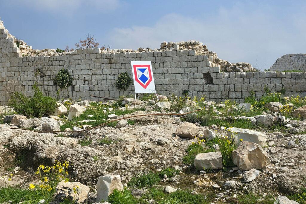 Damaged stone wall at a UNESCO heritage site in Tyre, Lebanon, with a UNITAR/UNOSAT damage assessment marker in the foreground.
