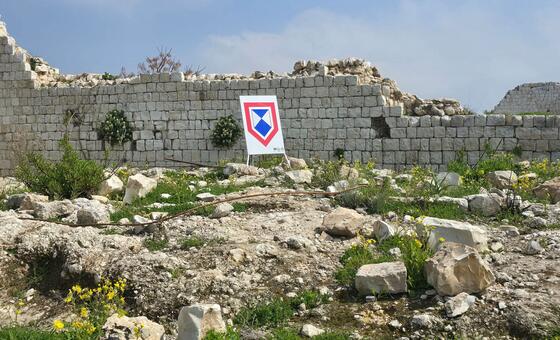 Damaged stone wall at a UNESCO heritage site in Tyre, Lebanon, with a UNITAR/UNOSAT damage assessment marker in the foreground.