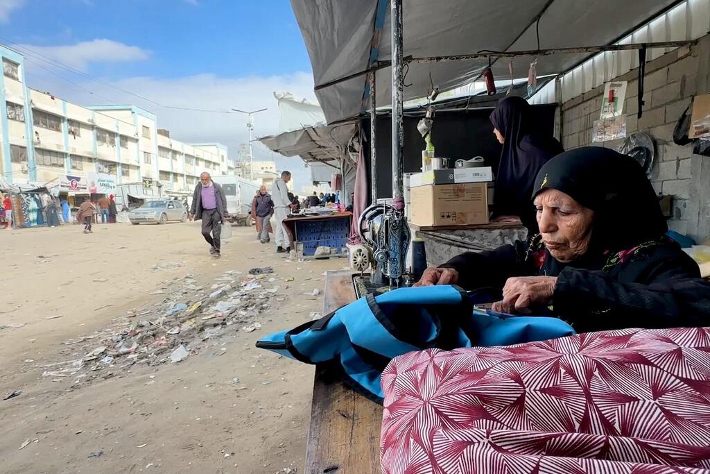تجلس السيدة الفلسطينية المسنة، نغين بن عيسى، أمام ماكينة خياطة في شارع جلال في خان يونس، غزة، لإصلاح الملابس ودعم أسرتها بعد انقطاع المساعدات الاجتماعية بسبب الاضطرابات الناجمة عن الحرب.