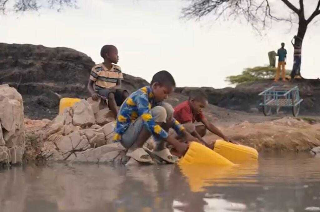 Watoto nchini Tanzania wakikusanya maji kutoka chanzo cha maji ya asili wakitumia makopo ya manjano.