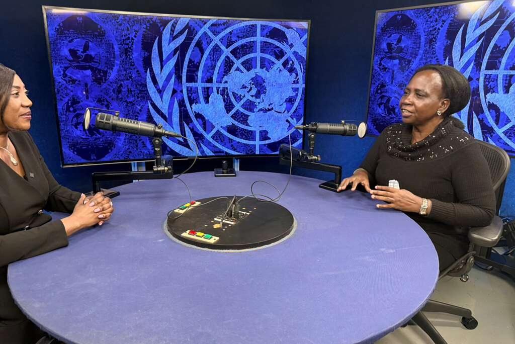 Wanawake weusi wawili wameketi kwenye meza ya mviringo katika studio ya redio, wakizungumza kwa kutumia maikrofoni. Nyuma kuna skrini kubwa zinazoonyesha nembo ya UN Women kwa rangi ya bluu.