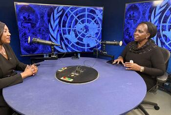 Wanawake weusi wawili wameketi kwenye meza ya mviringo katika studio ya redio, wakizungumza kwa kutumia maikrofoni. Nyuma kuna skrini kubwa zinazoonyesha nembo ya UN Women kwa rangi ya bluu.