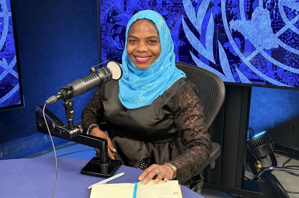 Mwanamke katika hijab ya bluu akizungumza kwenye kipaza sauti cha studio dhidi ya background ya bluu.