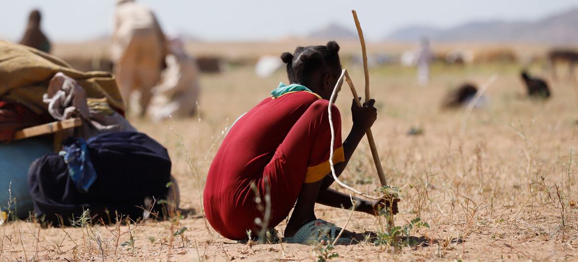 A young girl in a red shirt digs holes in the dry earth to create shelter for her family in a displacement camp in Tawila, Sudan, following violence in Al Fasher.