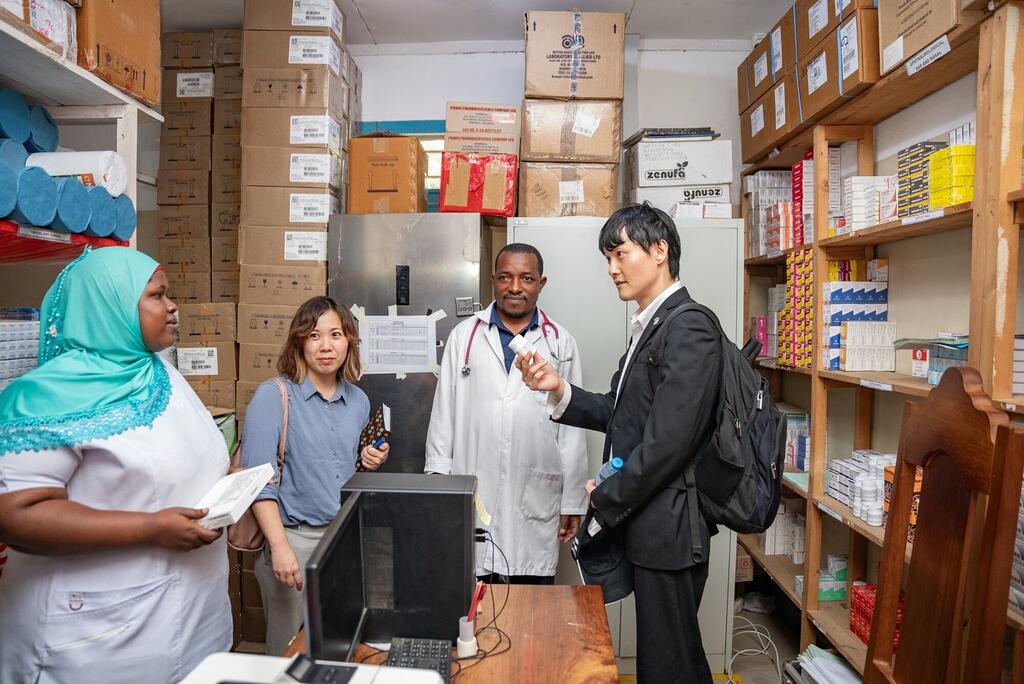 Kikundi cha wafanyakazi wa afya na wageni katika ghala la vifaa vya matibabu huko Mwanza, Tanzania, wakijadili huduma za afya chini ya mpango wa STEPPS.