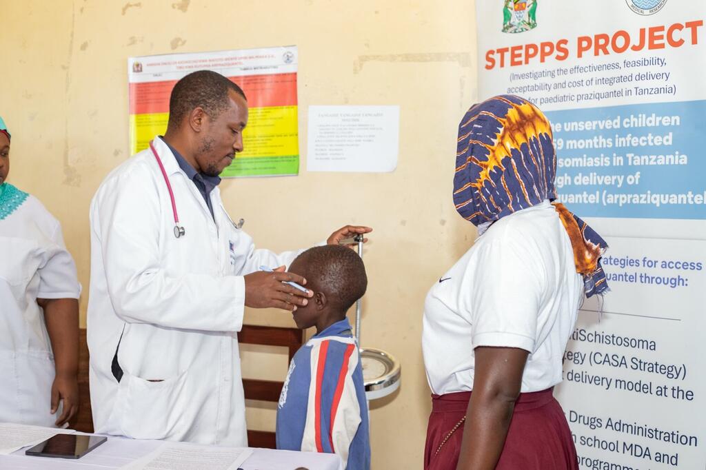 Mfanyakazi wa huduma ya afya katika koti nyeupe anaangalia sikio la mtoto mchanga wakati wa uchunguzi wa matibabu kama sehemu ya Mradi wa STEPPS huko Mwanza, Tanzania, unaolenga kutoa huduma za afya kwa watoto.