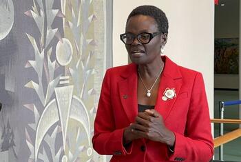Mwanamke mweusi amevaa blazer nyekundu, miwani, na mkufu wa lulu akizungumza.