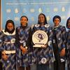 Wanawake sita, wakiwemo mahakimu wa Tanzania, wanapiga picha kwenye hafla ya CSW70. Mwanamke mmoja ana bamba la tuzo kwa Chama cha Mahakimu wa Wanawake wa Tanzania. Nyuma ina nembo za UN na kampeni 'Stop. Prevent. Protect.'