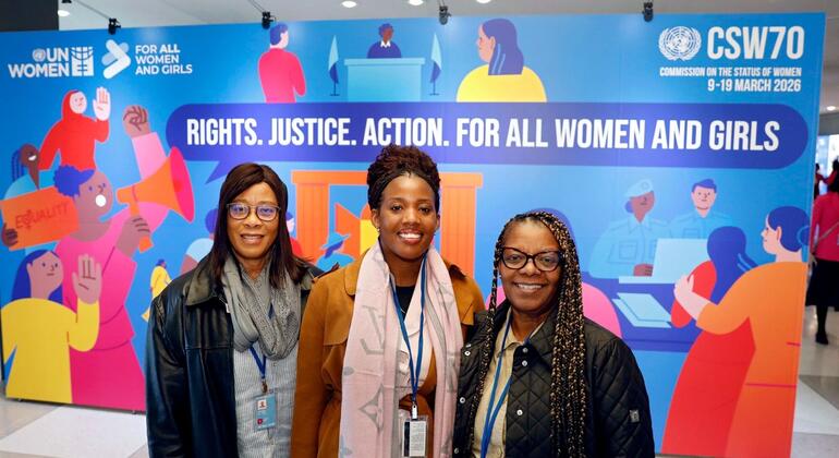 Wanawake weusi watatu wenye tabasamu wakipiga picha mbele ya bendera ya UN Women CSW70 ya rangi ya bluu.