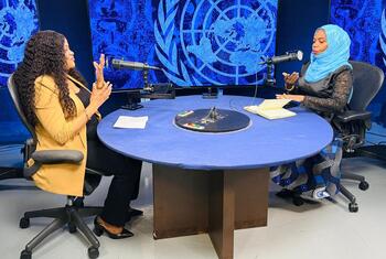 Wanawake wawili wameketi kwenye meza ya mviringo yenye rangi ya bluu wakiwa na maikrofoni, wakirekodi podcast katika studio yenye alama ya Umoja wa Mataifa.