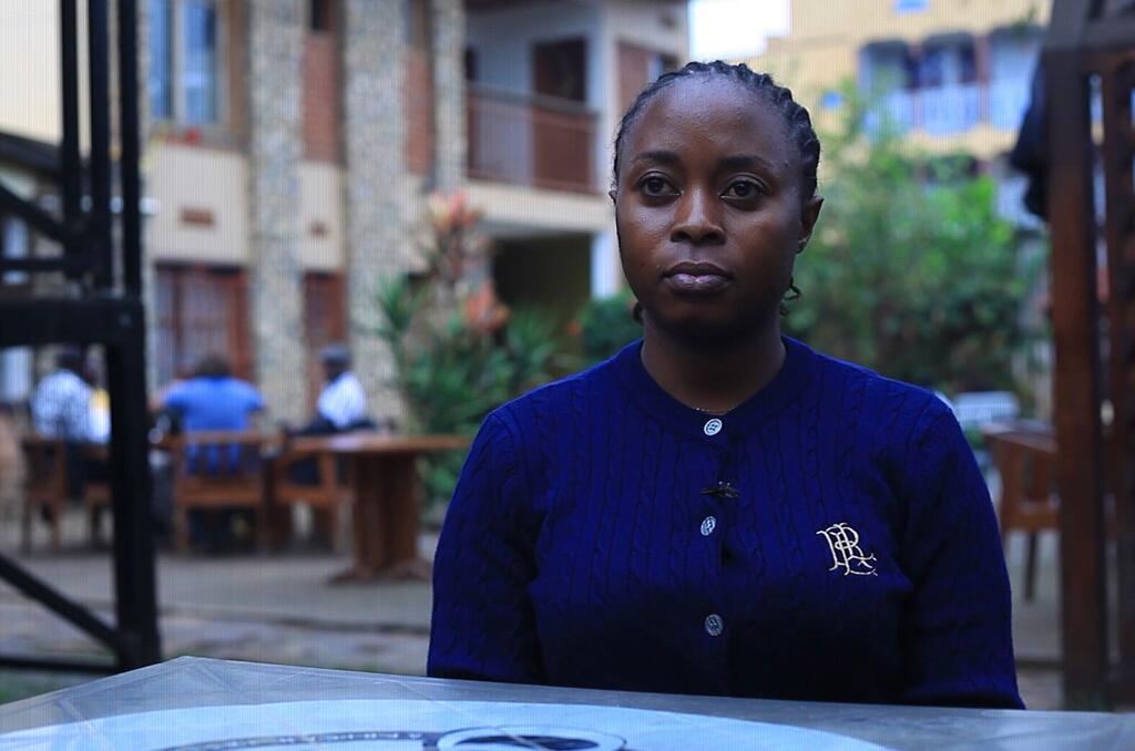Picha ya mwanamke mwenye ngozi nyeusi na nywele zilizopambwa, amevaa cardigan ya bluu, akitazama kamera wakati wa tukio nchini DR Congo.