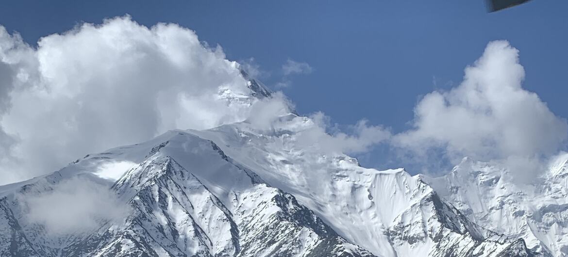 Величественный вид на заснеженные горные вершины и ледники в Таджикистане, с белыми облаками, дрейфующими по голубому небу.