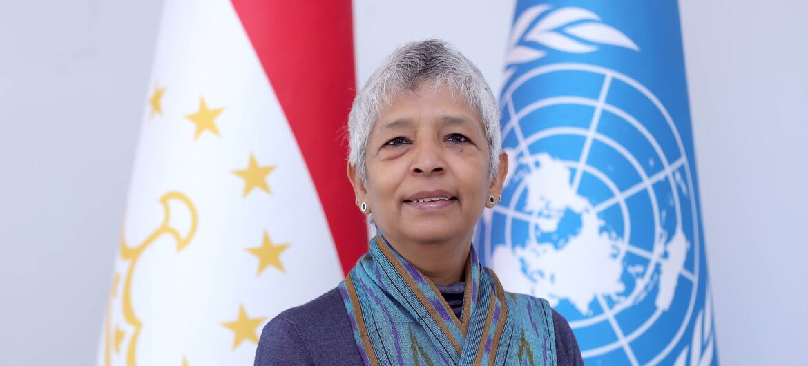 Портрет женщины с короткими седыми волосами, стоящей перед флагами Таджикистана и ООН.
