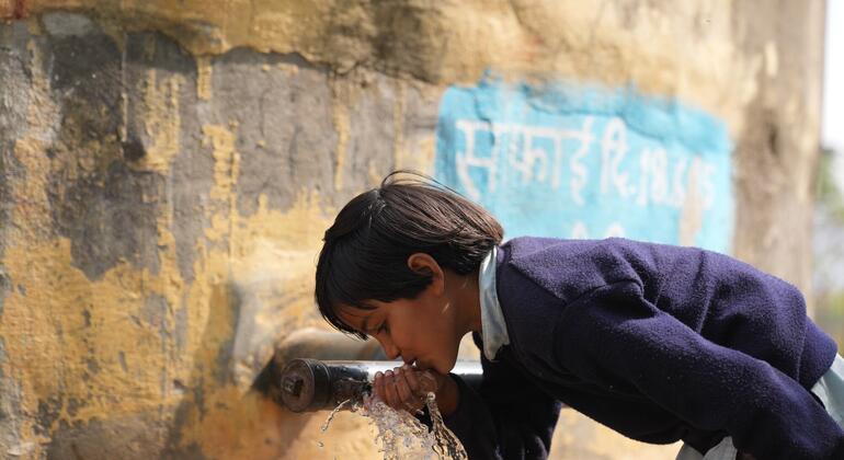 Сара, молодая индийская школьница в голубой униформе, пьет воду из металлического крана за пределами своей школы в деревне Адол, штат Раджастан.