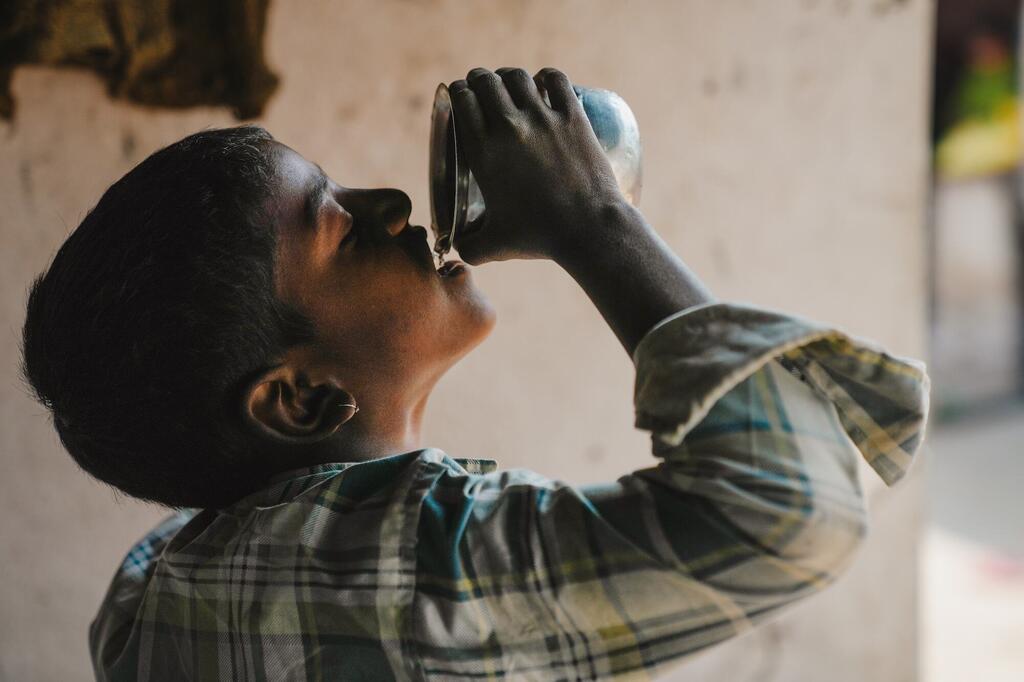 Un joven indio bebiendo agua de un vaso de metal, representando el impacto de las iniciativas de seguridad hídrica.