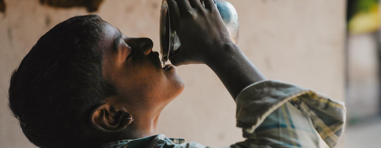 Um jovem indiano bebendo água de um copo de metal, representando o impacto das iniciativas de segurança hídrica.