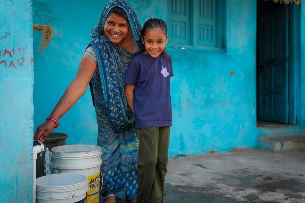 Shanti Bai et sa fille Garima dans le village de Kotdi, dans le Rajasthan, en Inde, souriant alors qu'elles collectent de l'eau potable d'un nouveau robinet domestique installé par le biais de la mission Jal Jeevan.