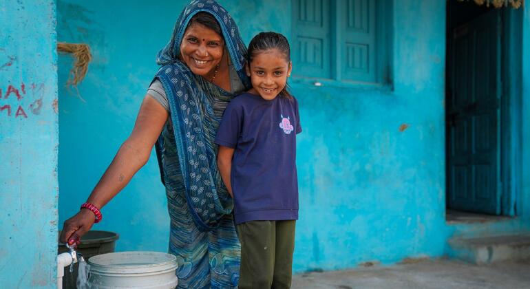 Shanti Bai e sua filha Garima na aldeia de Kotdi, em Rajasthan, Índia, com um sorriso enquanto coletam água potável de uma nova conexão de torneira doméstica instalada através da Missão Jal Jeevan.