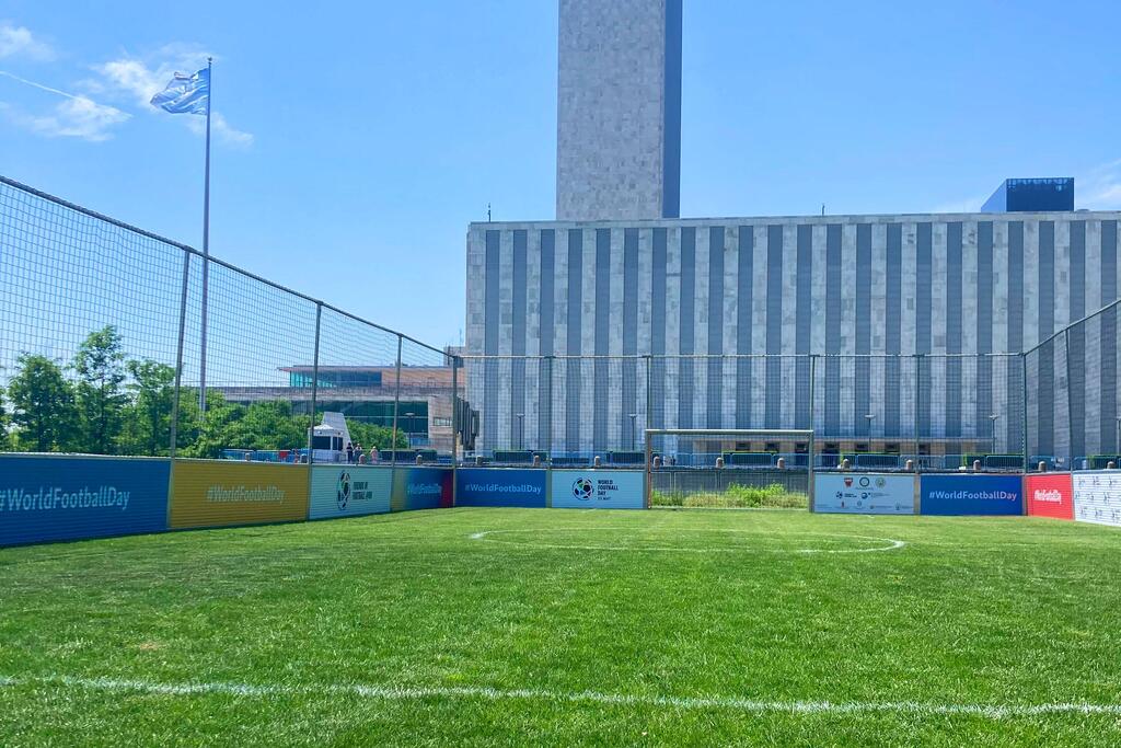 An empty soccer field at the United Nations Headquarters in New York, with a UN flag and World Football Day banners visible.