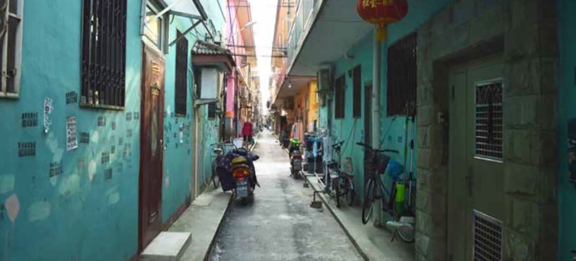 A narrow alleyway with colorful buildings in China, featuring parked scooters and bicycles.
