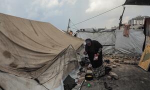 A woman standing outside a weathered tent prepares food. She stands in an area surrounded by makeshift tents and improvised shelters at a settlement in Gaza City.