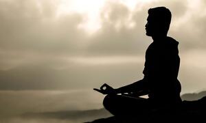 A man meditating in a peaceful mountain setting during sunset, silhouetted against the sky.