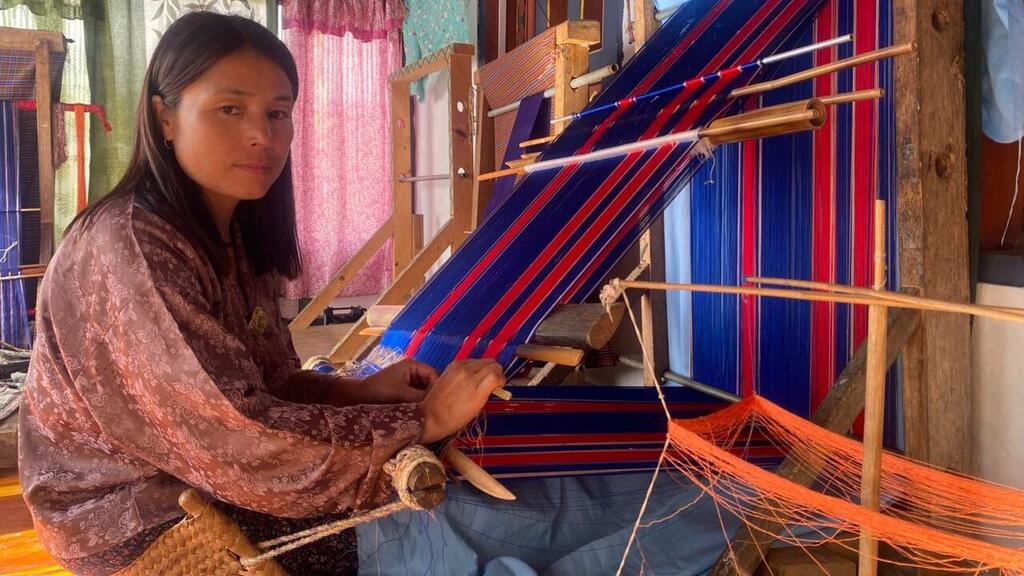 Бутанская женщина умело ткает красочную ткань на традиционной деревянной ткани.