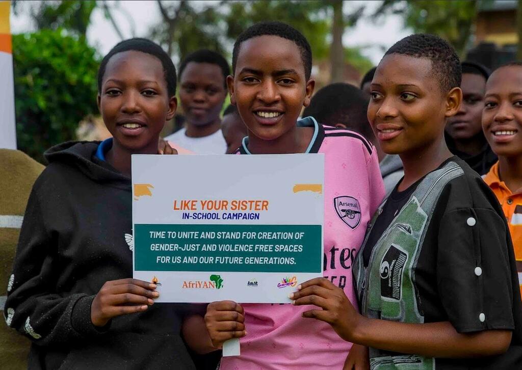 Wasichana watatu wenye tabasamu wakiwa na ishara kwa ajili ya kampeni ya 'Like Your Sister' shuleni wakipigania maeneo ya haki ya jinsia na yasiyo na vurugu katika shule.
