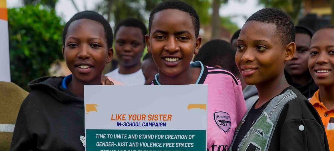 Três garotas sorridentes segurando um cartaz para a campanha "Like Your Sister" nas escolas, defendendo espaços sem violência e justiça de gênero nas escolas.