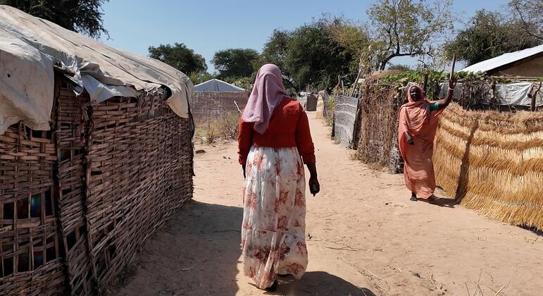 一位妇女在中非共和国的一个难民营里行走,另一位妇女在后台挥手.
