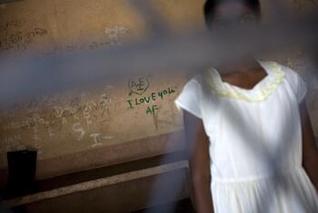 Una joven con un vestido blanco se encuentra frente a una pared cubierta de graffiti, incluyendo el mensaje 'YO TE AMO' escrito en verde.