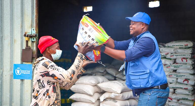 Funcionários do PMA em coletes azuis ajudando a descarregar sacos de ajuda alimentar de um contêiner em um centro de alojamento no distrito de Chokwe, Moçambique, após inundações que deslocaram mais de 700.000 pessoas.