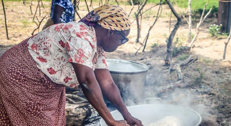Joana Maria João Chongo, de 71 anos, uma mulher afetada pelas inundações em Chókwè, Moçambique, cozinha farinha de milho em uma grande panela sobre uma fogueira aberta no centro de alojamento de Chiaquelane, destacando sua resiliência apesar dos repetidos deslocamentos por inundações.