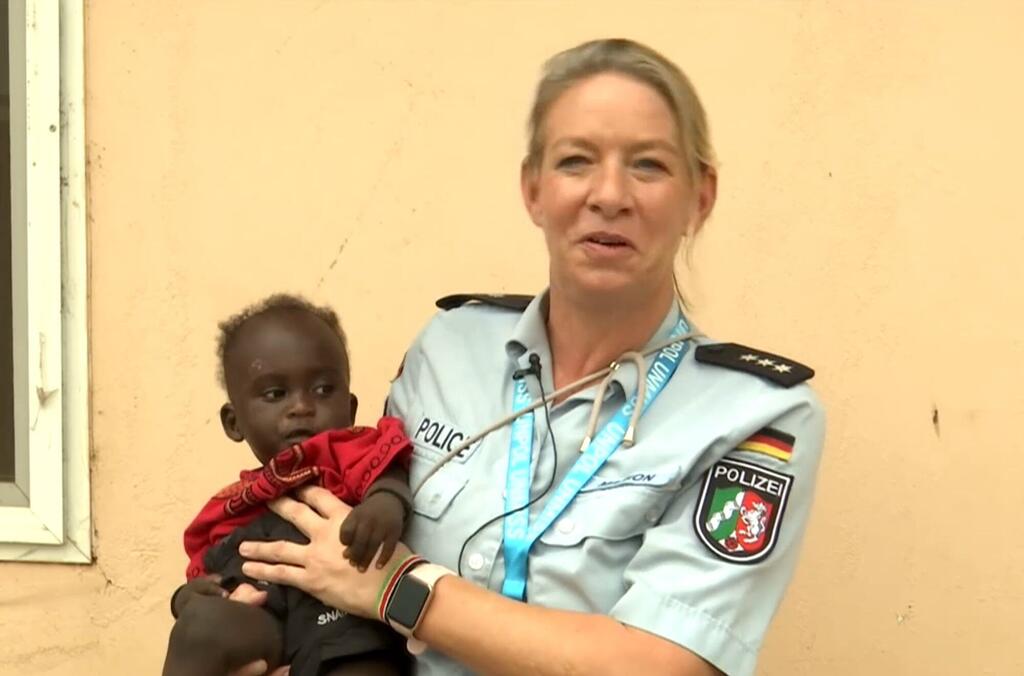 Afisa wa polisi wa Ujerumani kutoka UNMISS akishikilia mtoto mchanga katika nyumba ya watoto yatima huko Juba, Sudan Kusini, akikazia juhudi za kibinadamu kwa ajili ya haki za watoto.
