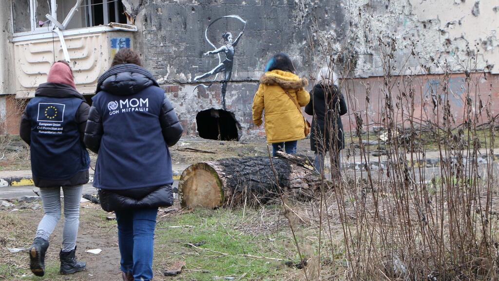 Quatre travailleurs humanitaires, dont deux de l'Union européenne pour la protection civile et l'aide humanitaire, passent devant un bâtiment endommagé avec un graffiti en style Banksy d'une ballerine.