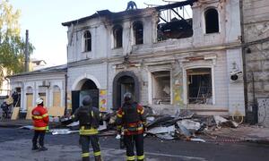 Bomberos en Ucrania inspeccionan un edificio muy dañado después de un incidente de conflicto, rodeado de escombros y destrucción.