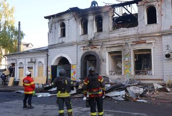 Bomberos en Ucrania inspeccionan un edificio muy dañado después de un incidente de conflicto, rodeado de escombros y destrucción.