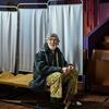 Un homme ukrainien âgé est assis sur un lit dans un refuge transformé en théâtre, entouré de rangées de sièges vides et d'écrans de protection de la vie privée, soulignant la crise humanitaire causée par la guerre en cours.