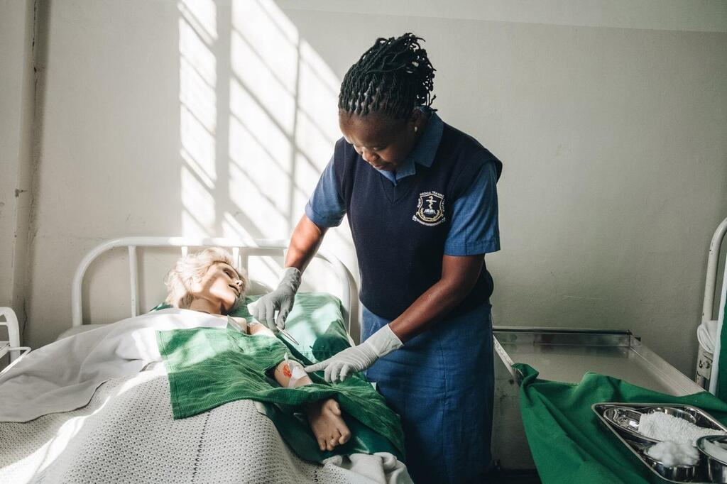 Mfanyakazi wa huduma za afya nchini Kenya, anayehusishwa na KMTC na WHO, anafanya utaratibu wa matibabu kwa mgonjwa katika kitanda cha hospitali.