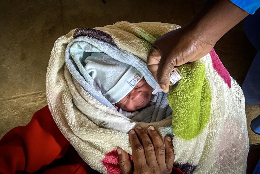 Mfanyakazi wa afya anampa chanjo ya polio mtoto mchanga anayelala akiwa amefungwa katika blanketi yenye rangi mbalimbali nchini Malawi, kama sehemu ya kampeni ya chanjo ya WHO Afrika.
