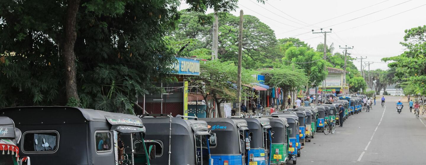 A long line of colorful autorickshaws waits on a paved road in Sri Lanka to refuel during a fuel shortage crisis.