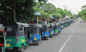 A long line of colorful autorickshaws waits on a paved road in Sri Lanka to refuel during a fuel shortage crisis.