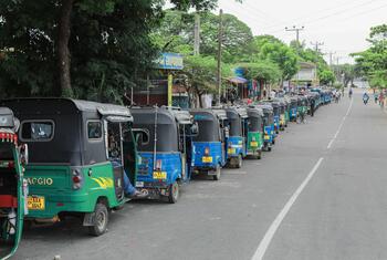 A long line of colorful autorickshaws waits on a paved road in Sri Lanka to refuel during a fuel shortage crisis.
