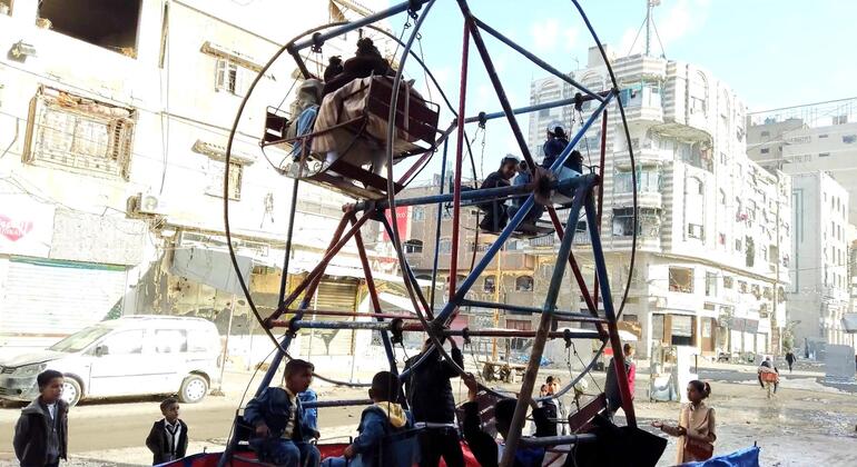 أطفال فلسطينيون يحتفلون بعيد الفطر ويلعبون على الأراجيح في وسط مدينة غزة، ويمكن رؤية المباني المتضررة في الخلفية.