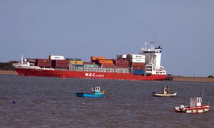 A large cargo ship carrying shipping containers on the water, alongsid three smaller boats.