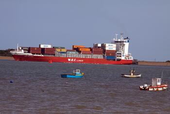 A large cargo ship carrying shipping containers on the water, alongsid three smaller boats.