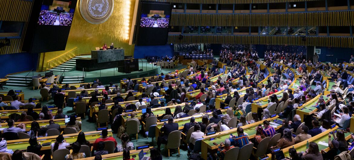 A wide view of the United Nations General Assembly hall during the opening of the Permanent Forum on Indigenous Issues (UNPFII). The room is filled with attendees seated at curved desks, facing a central podium under the large UN emblem.